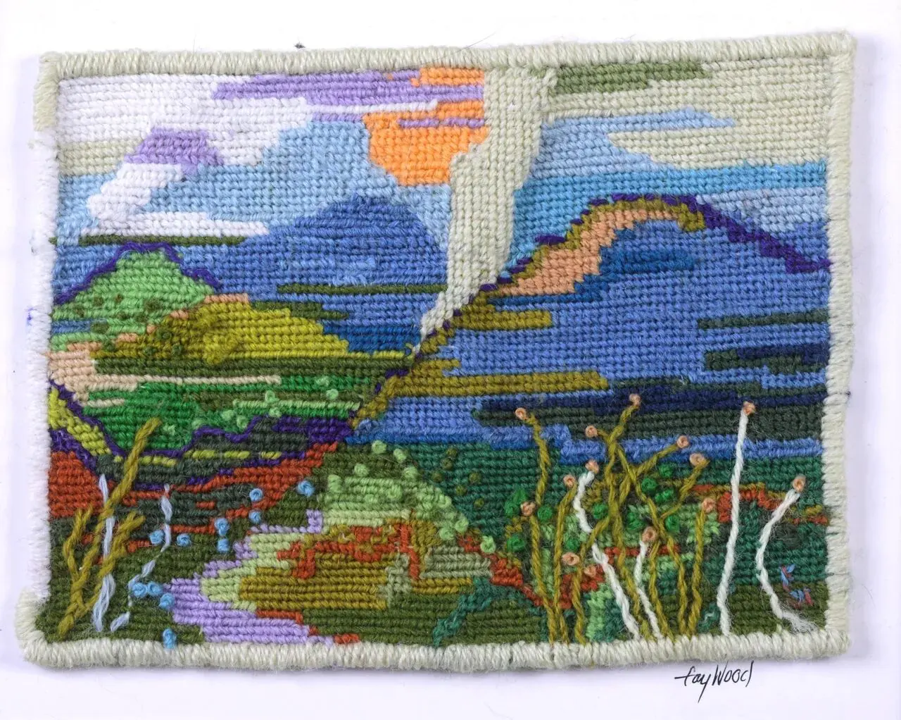 Colorful embroidered landscape with sky and mountains.